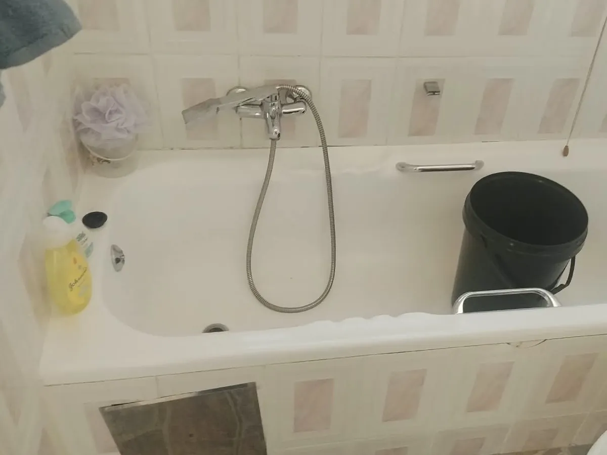 Bath mixer tap with a hand shower fitted above a white bath