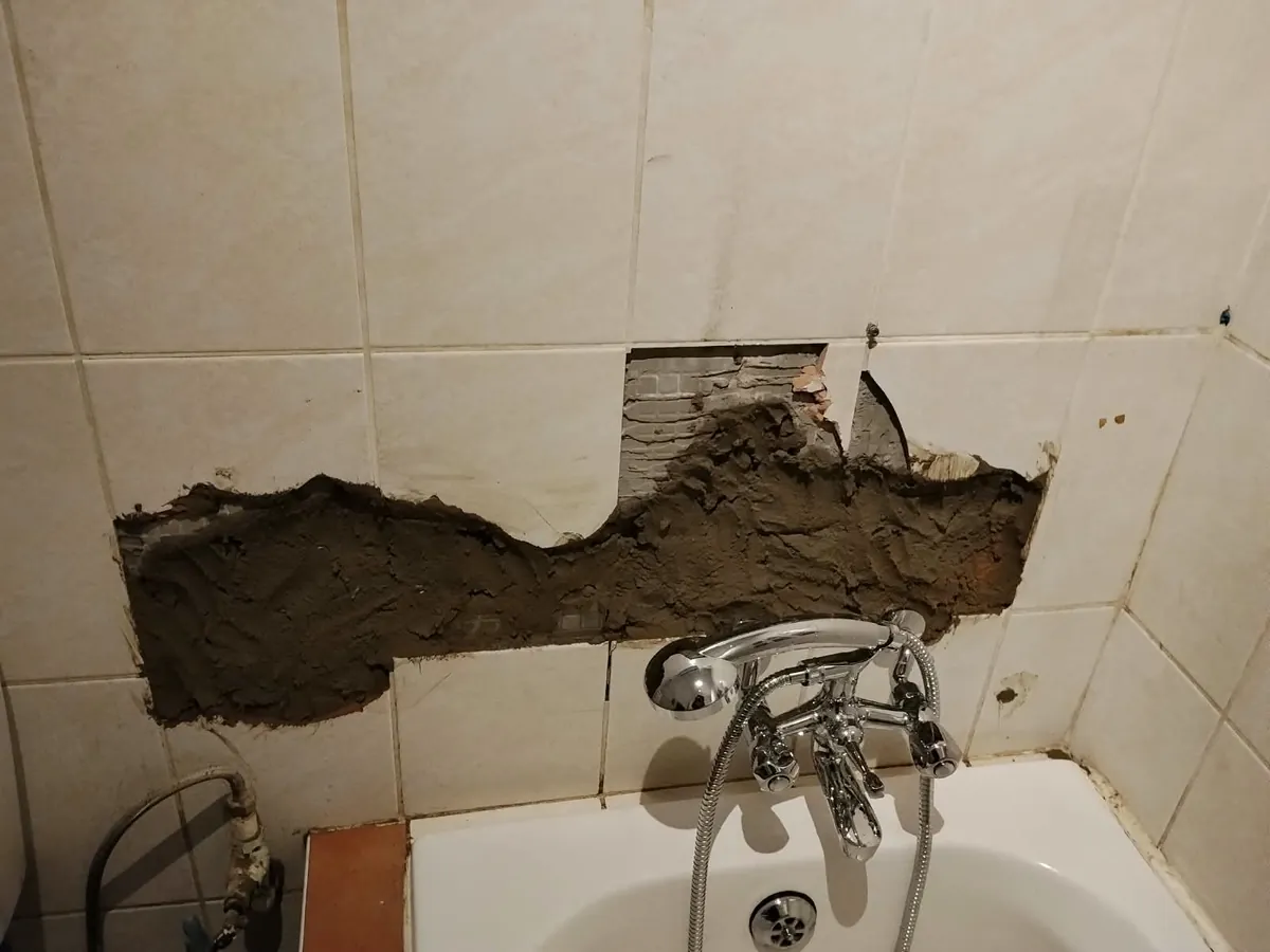 Bathroom wall above a bath mixer with tiles removed and the opening filled with fresh plaster