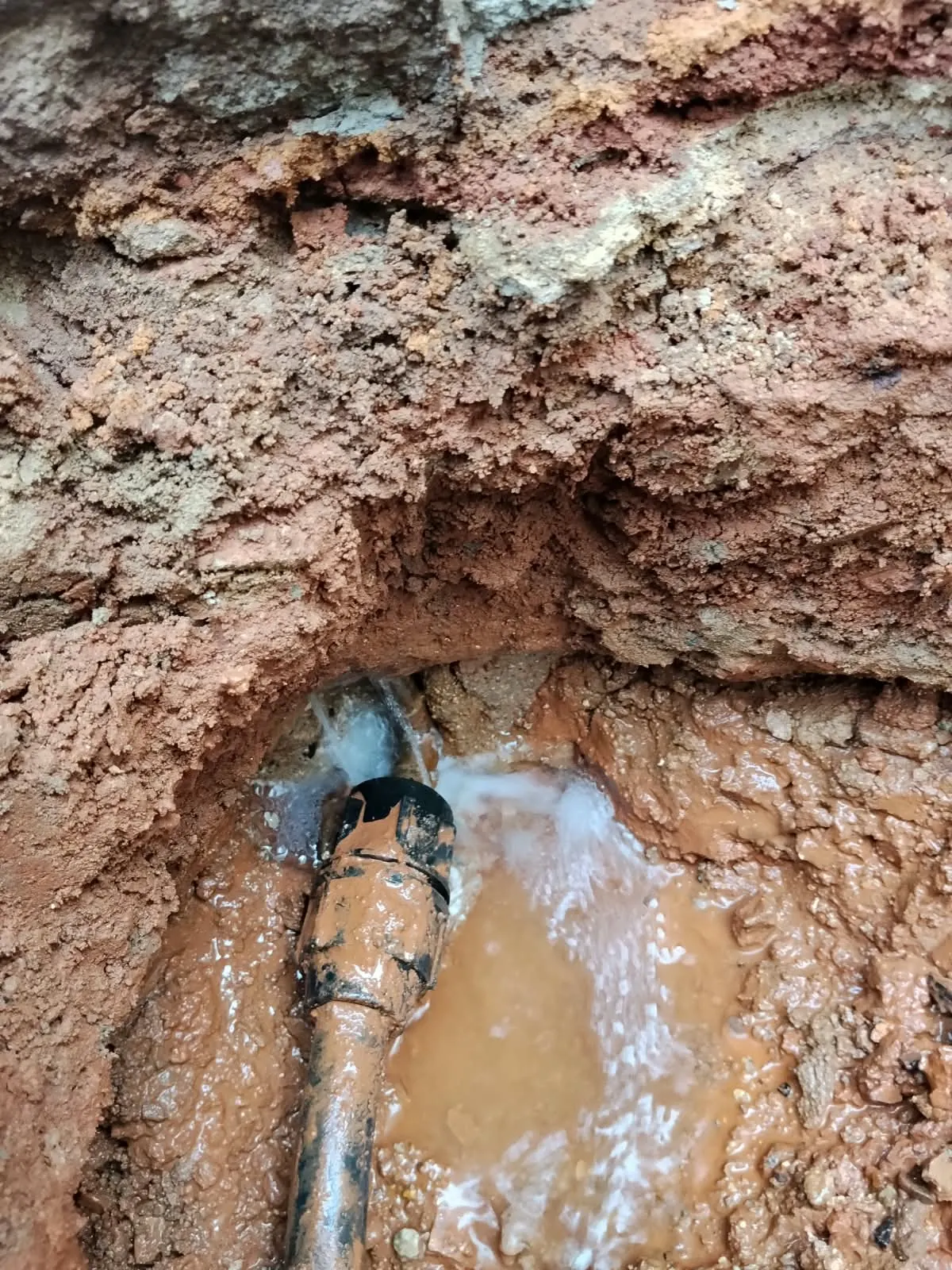 Water spraying from a burst underground pipe exposed in a trench