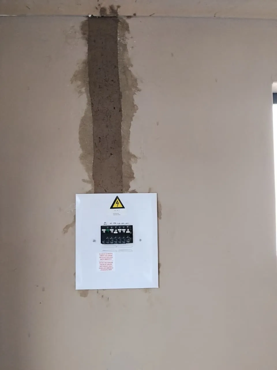 Distribution board with its white cover fitted and the wall chase above it plastered closed