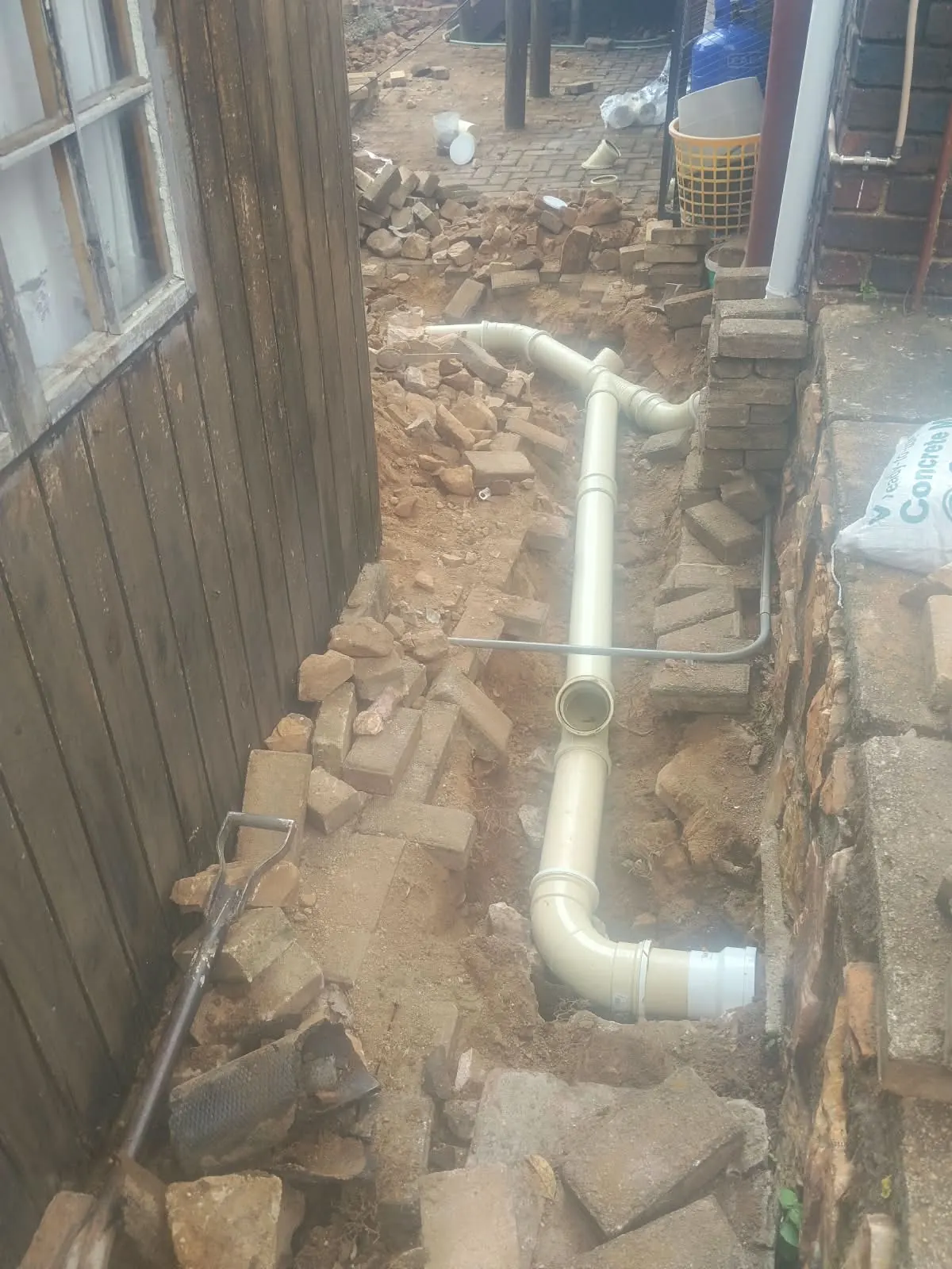 New drain pipe laid in an open trench beside a house
