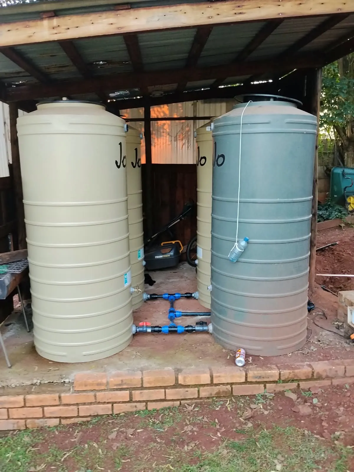 Four JoJo water tanks linked together with pipes and valves under a carport