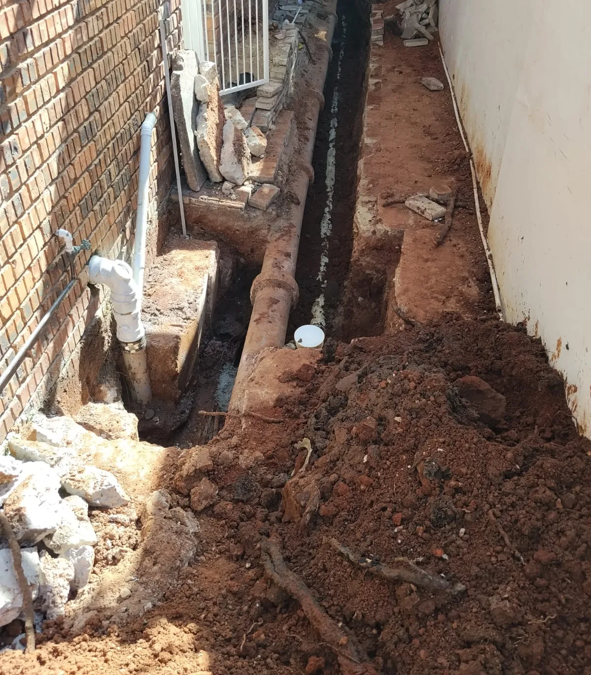 Old underground drain line dug open in a trench alongside a brick house