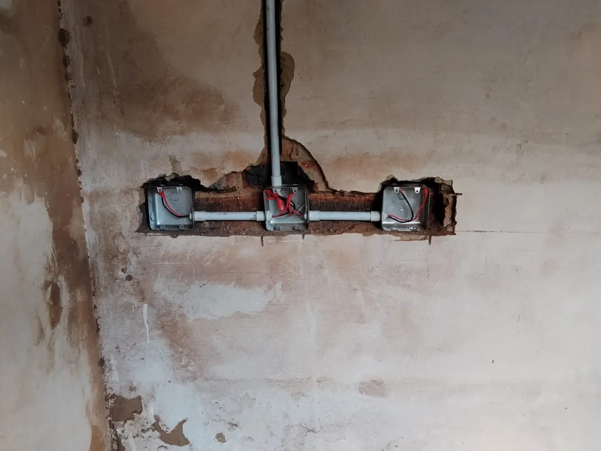 Three metal wall boxes joined by conduit, chased into a plastered wall