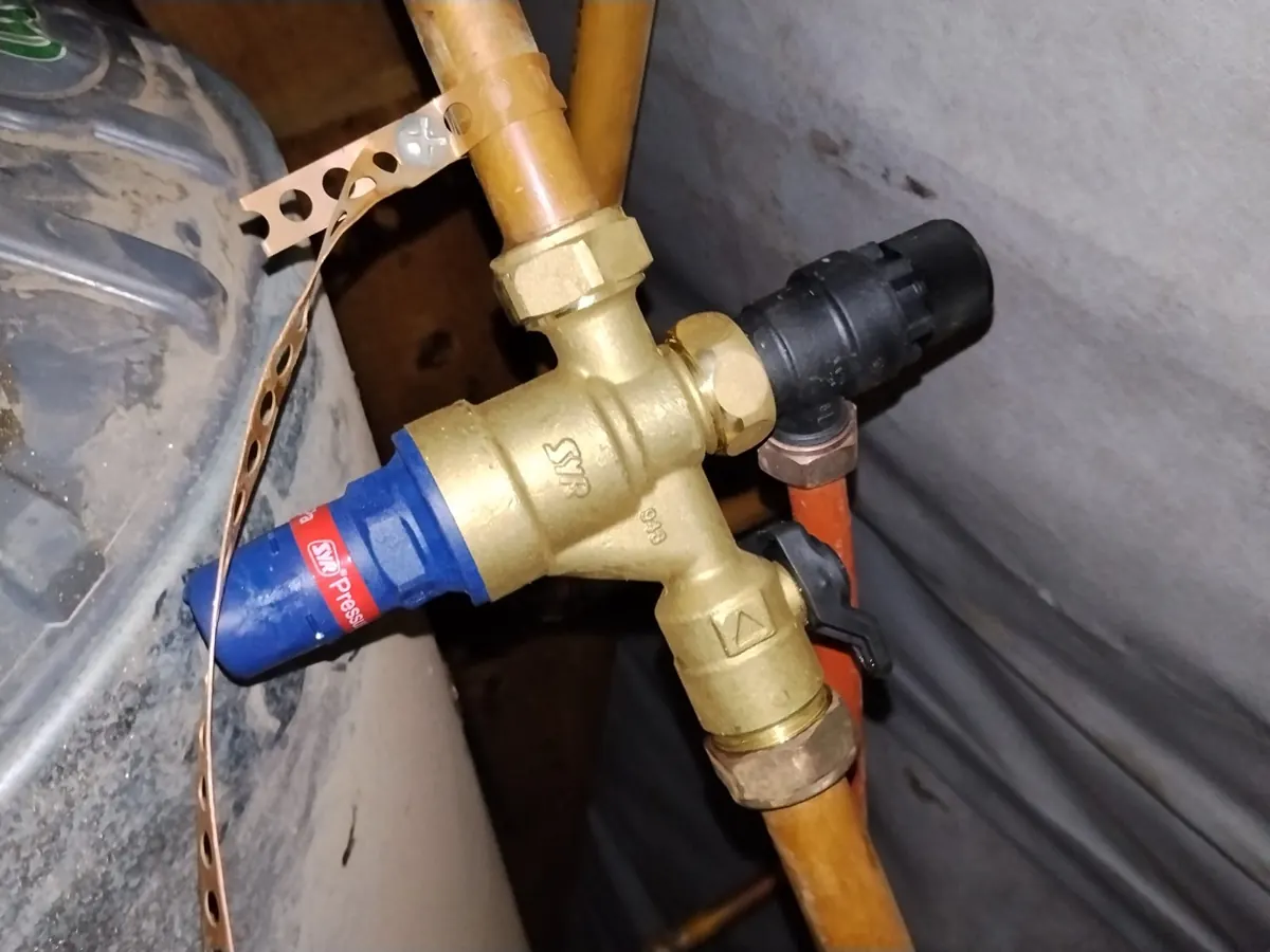 New brass pressure control valve fitted on copper pipes next to a geyser