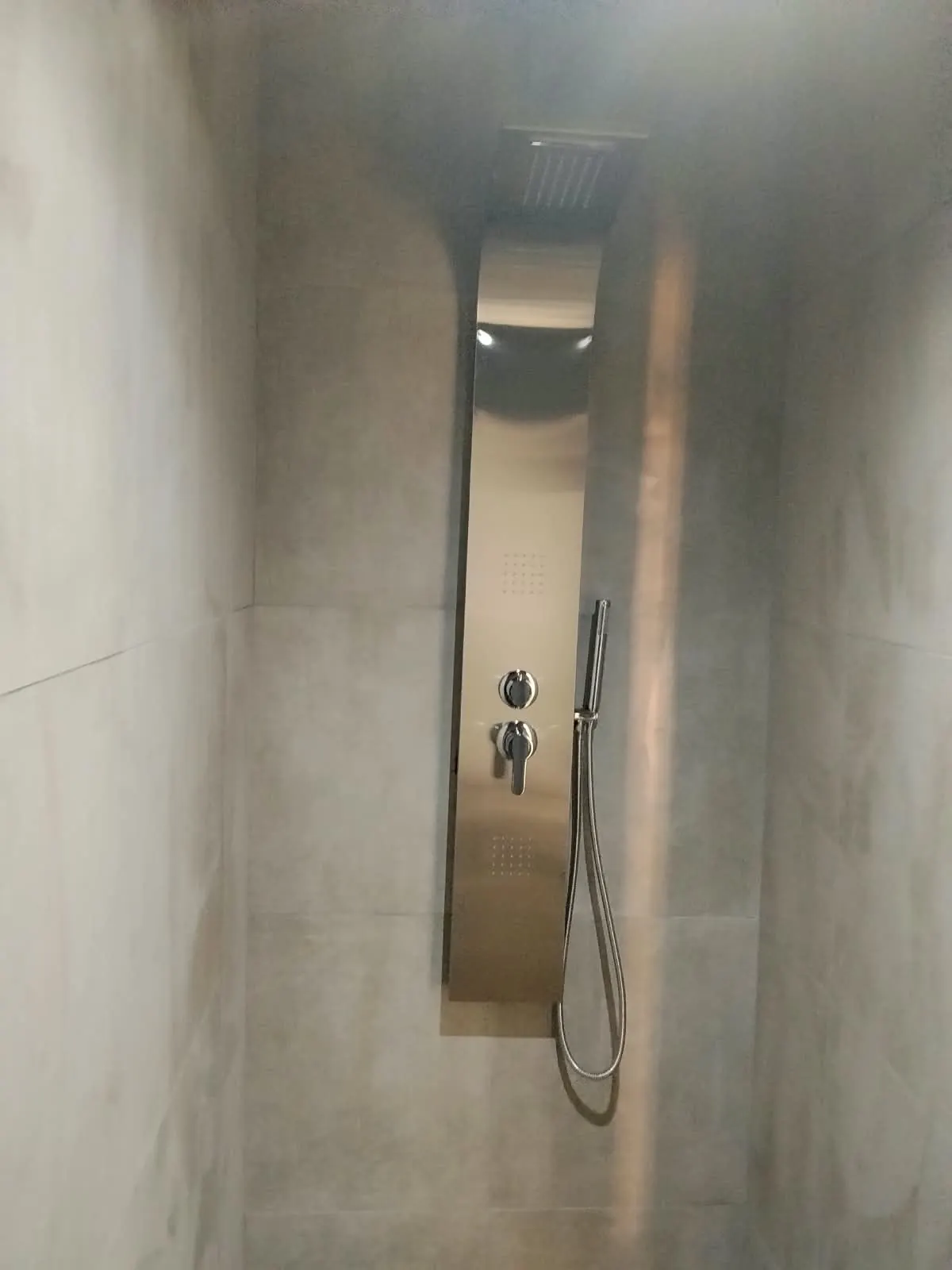 Stainless steel shower panel with hand shower fitted in a tiled shower
