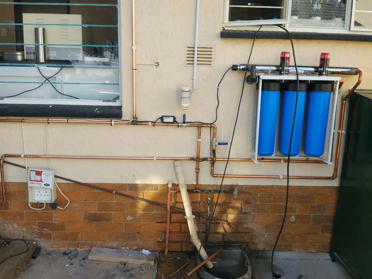 Three-stage water filter with UV unit connected with copper pipes along an outside wall