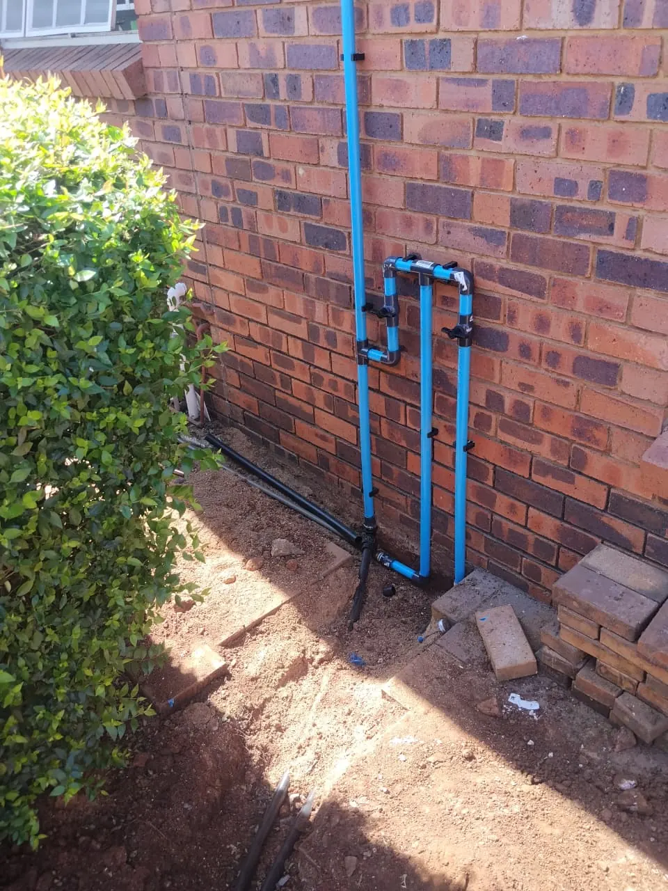 New blue water pipes clipped neatly to a face-brick wall